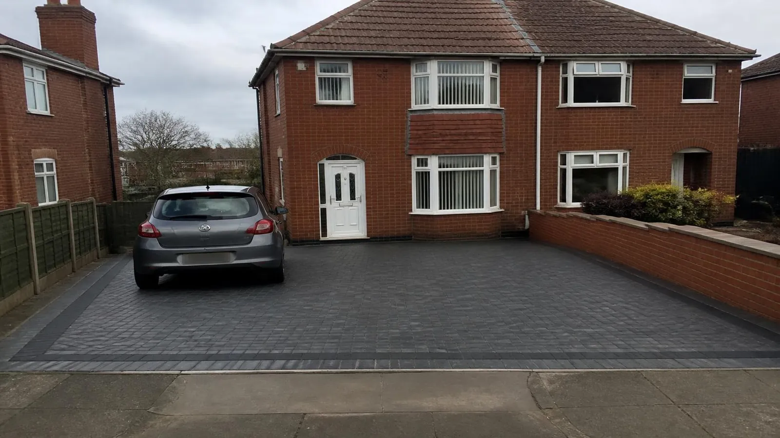 Example image: block-paved driveway in grey blocks with a charcoal border in front of a brick house