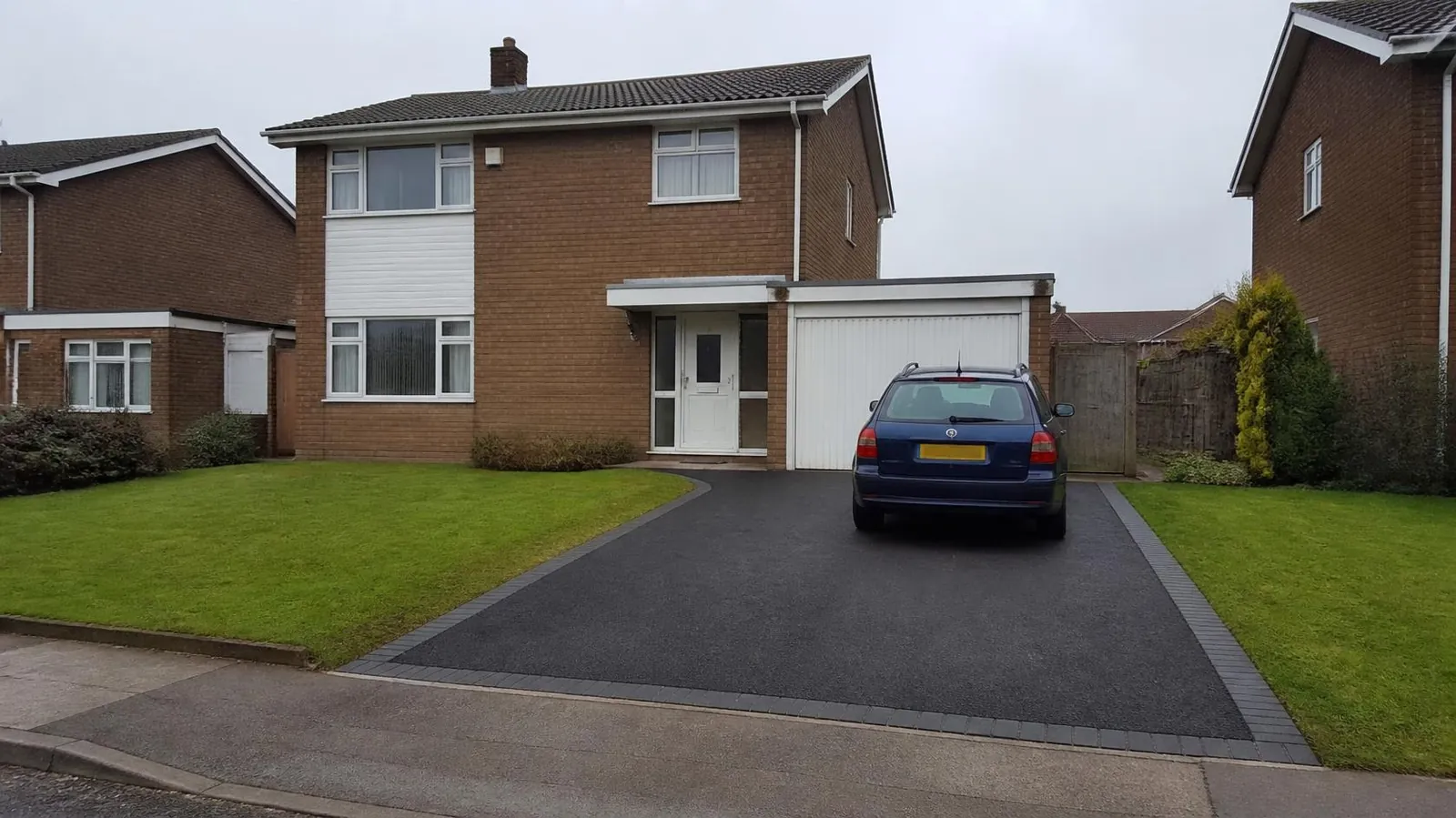 Example image: 1970s detached house with a tarmac drive, block border and open-plan lawn